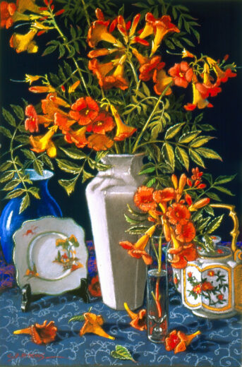 Orange trumpet flowers in a white slender vase. Other ceramic pieces also.