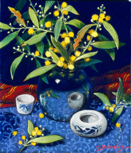 A small blue vase contains bright yellow ball flowers. Other ceramic pieces and the tablecloth are shown as reflected in the blue vase.